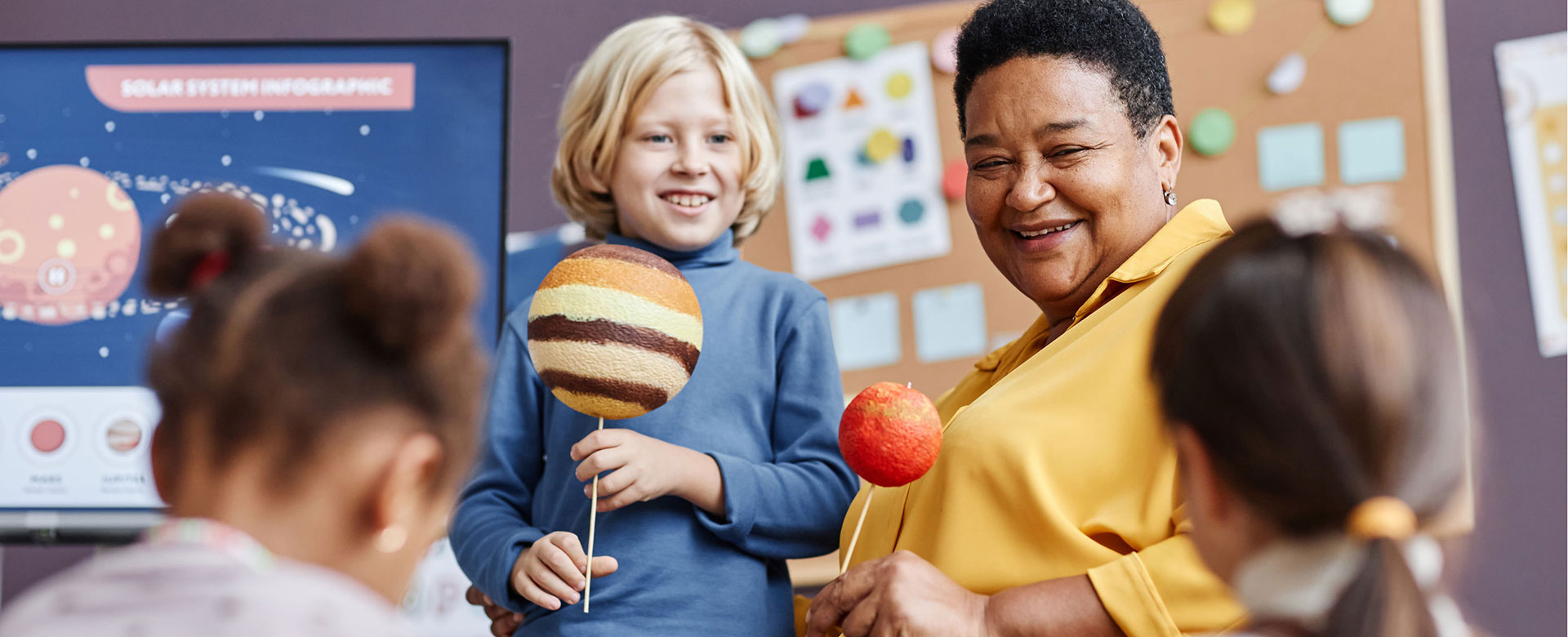 Teacher and little boy with planet models during discussion of solar system at lesson in kindergartenlding planet at young students with solar system graphic in kindergarten