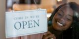 Microbusiness owner putting up sign saying "Come in. We're Open." with the Arizona Office of Economic Opportunity logo on the side